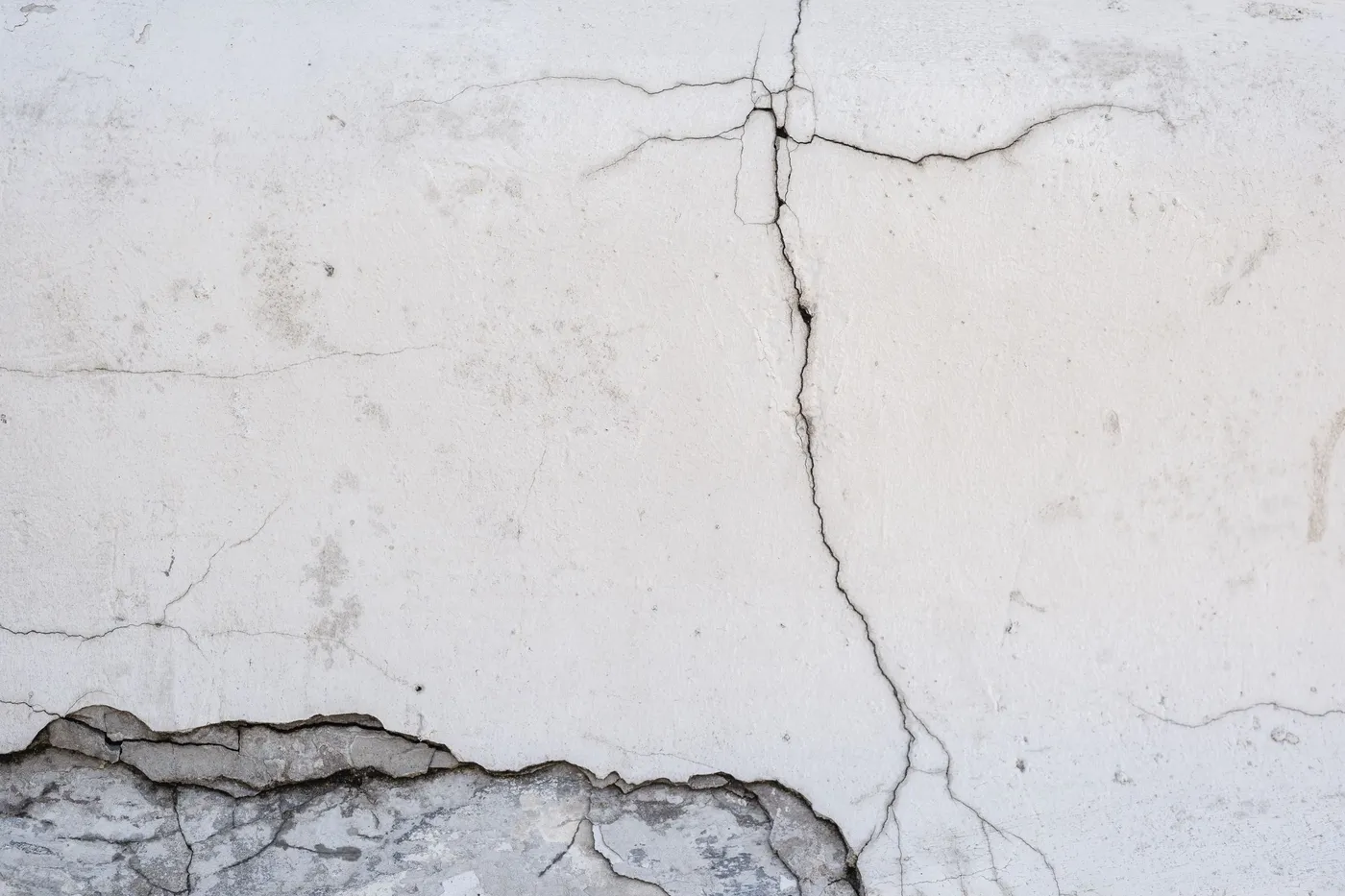 Close-up of a vertical crack running down a white-painted concrete wall, meeting a horizontal crack and a section of spalled concrete along the base