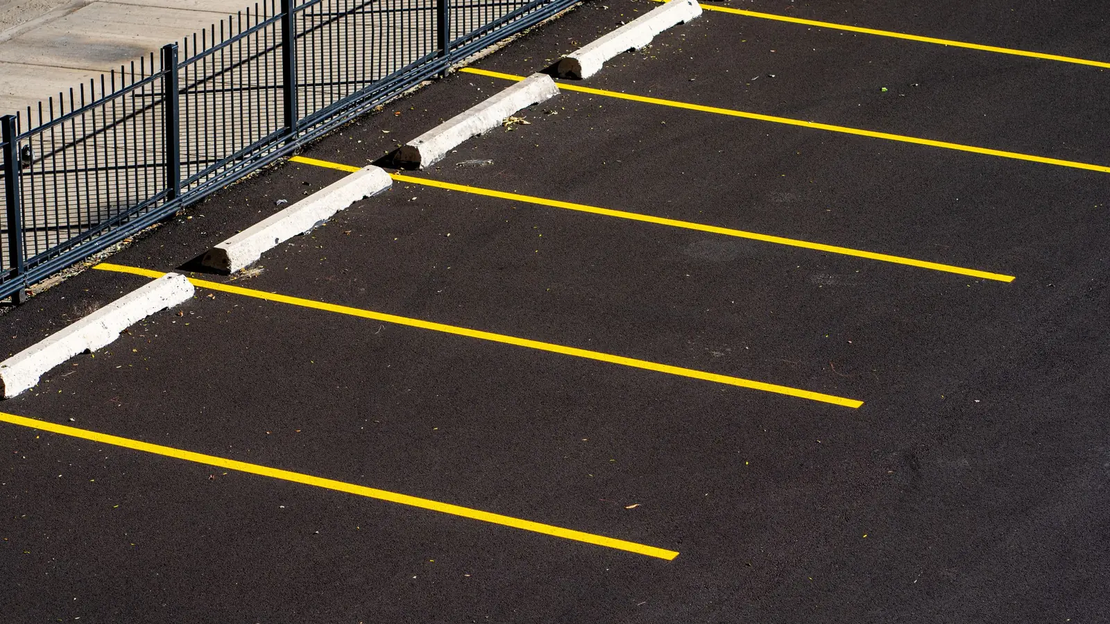 Freshly painted bright yellow parking stall lines running in rows across clean black asphalt, with white-painted concrete wheel stops at the head of each space